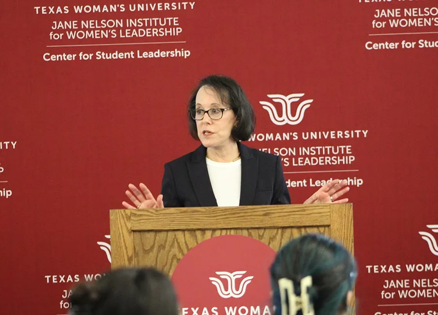 a woman speaks at a podium with the TWU Center for Student Leadership logo on a backdrop behind her.
