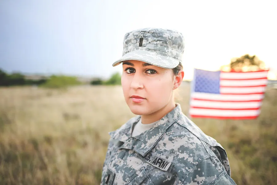 A woman in Army fatigues stands with an American flag in the background