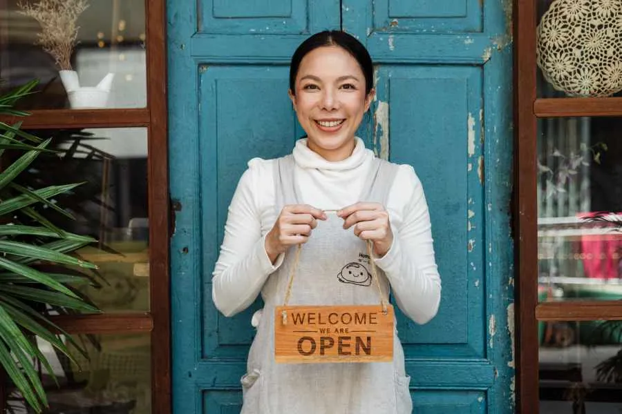 woman entrepreneur holding a sign that says: welcome we are open