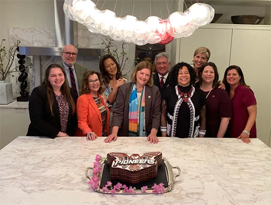 TWU Board of Regents posing with a cake decorated with the Pioneers logo