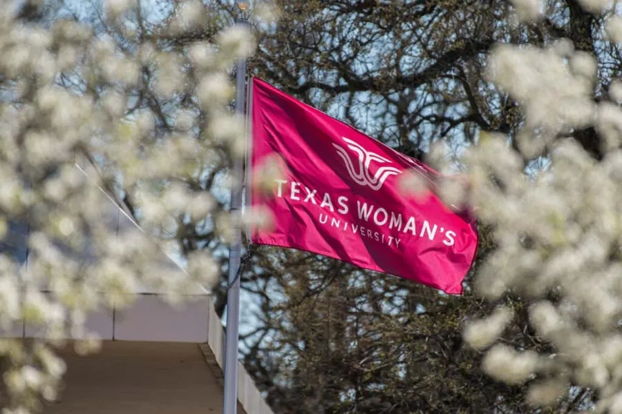 The TWU flag flutters in the breeze among the Denton campus' redbud blooms