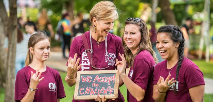 Chancellor Feyten makes the TWU hand sign with 3 students