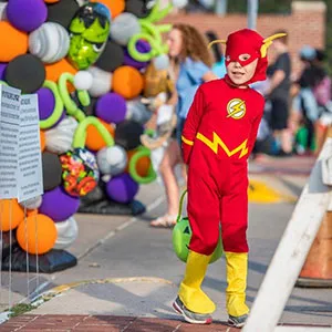 a little boy in a superhero costume stands outside the TWU student union building
