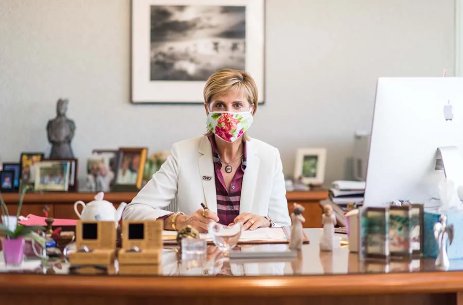 Chancellor Carine Feyten sits at her desk wearing a protective face mask