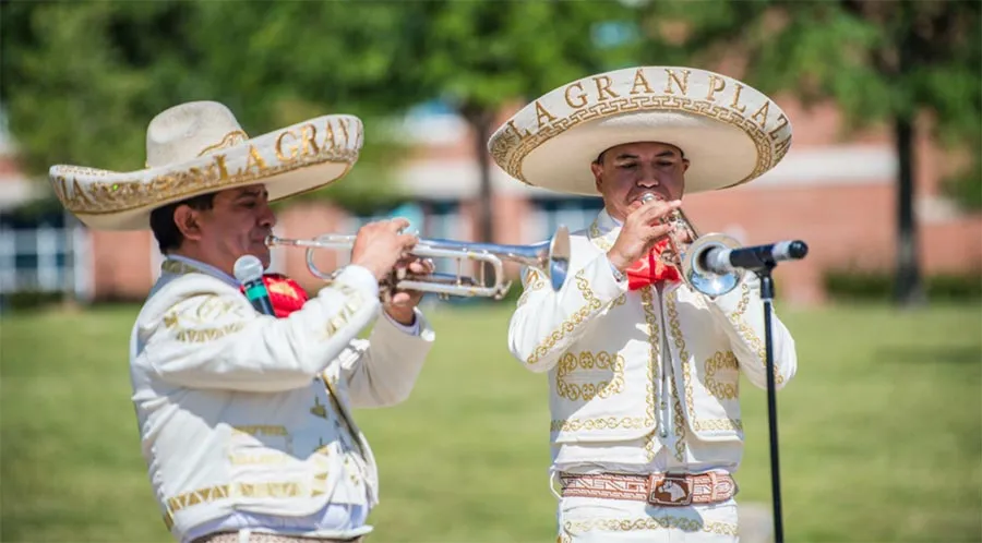 Two mariachi performers in full costume play trumpets out on the TWU Denton campus grounds.