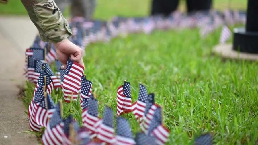 a sleeve in military camo plants a small American flag into the ground filled with many similar flags