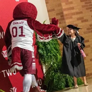 TWU mascot Oakley gives a young girl in cap and gown a high five