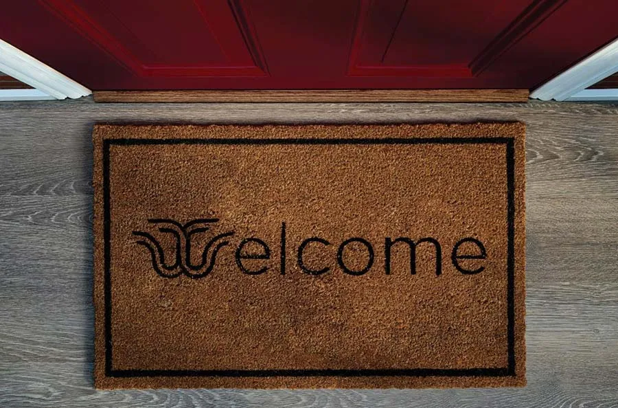 A welcome mat in front of a maroon door with the word 'welcome' that has the TWU logo as the W