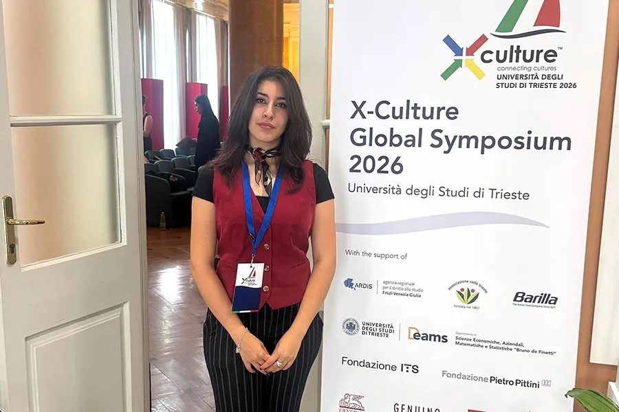 MAK student Alexa Norman stands next to a X-Culture Symposium banner