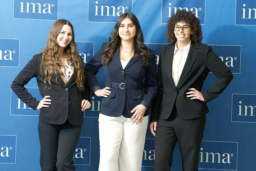 three MAK College students stand in business attire in front of a IMA blue backdrop