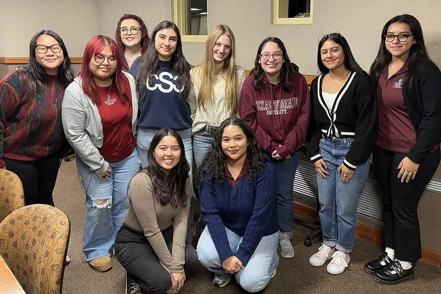 Eight business students stand in a conference room with two students crouching in front of them.