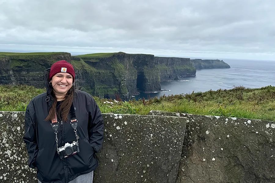 Jackie Farias with a camera around her neck stands in front of the Cliffs of Moher