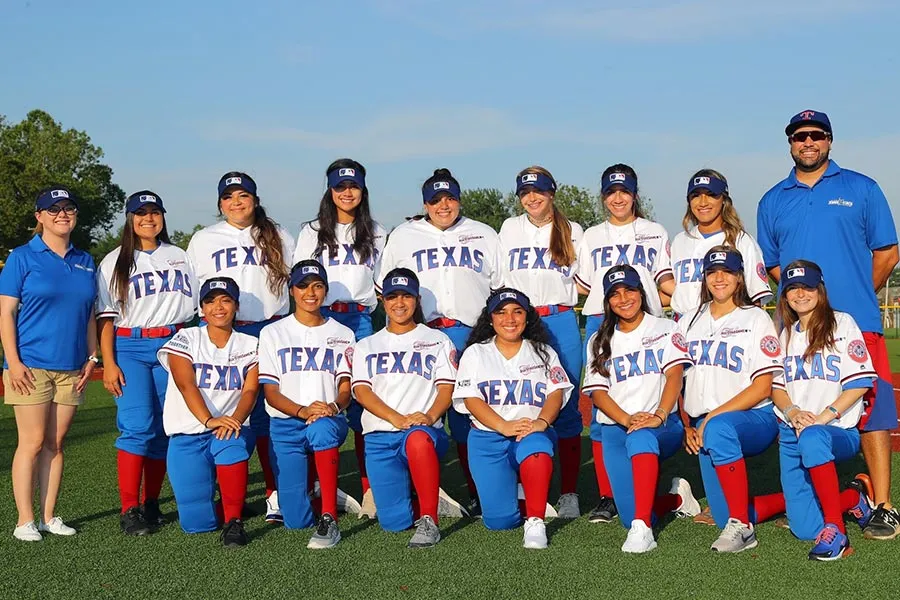 TWU alum Jesse Malone stands next to a team of softball players in a blue polo shirt