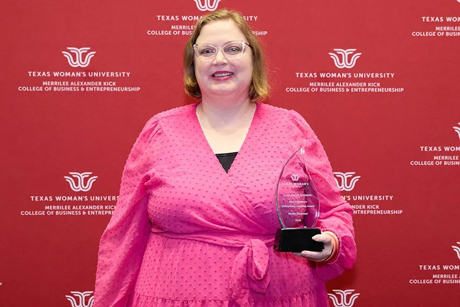 Molly Koerner holds a glass plaque in front of a maroon backdrop