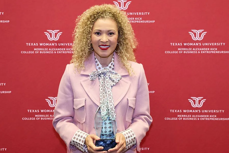 Sara Miller holds a glass plaque in front of a maroon backdrop