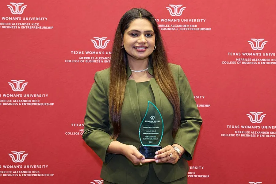 Shalini Kodial holds a glass plaque in front of a maroon backdrop
