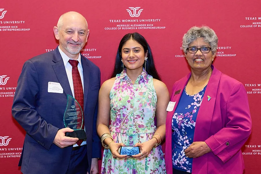 TWU student Sherley Malik stands with award next to David Rylander and Pushkala Raman in front of TWU backdrop