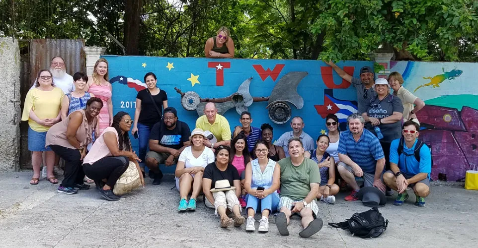 Dr. Rylander and Dr. Radighieri posing with students in front of a TWU painted wall in Cuba. 