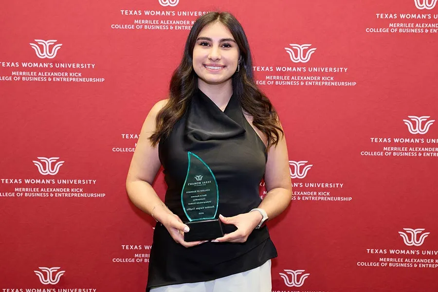 Romina holds a glass plaque standing in front of a maroon backdrop