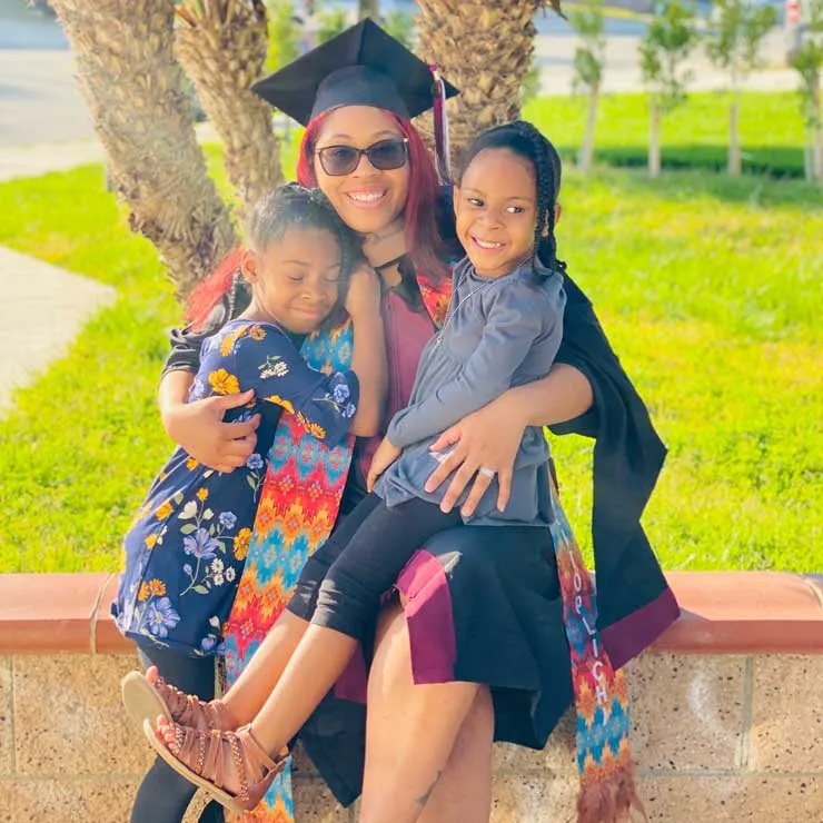 Kwashae Ruffin in academic regalia with two of her daughters on her lap.