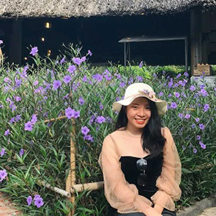 Nhi Chau sits outdoors with wildflowers behind her.