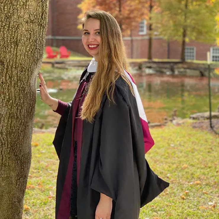 Regan Campbell in her academic regalia standing outdoors near the library on the TWU Denton campus.
