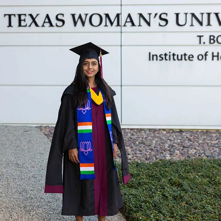 Sandhya Manjunath in academic regalia in front of the TWU Dallas campus.