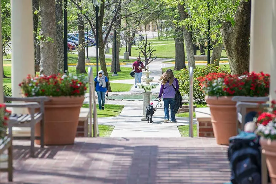 A woman walks across campus with her guide dog.