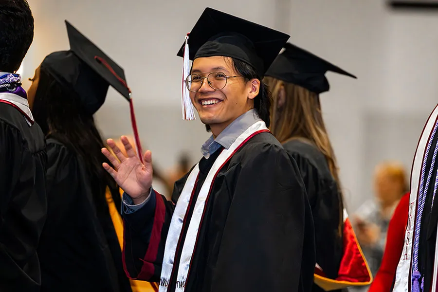 A graduate smiles and waves at the camera