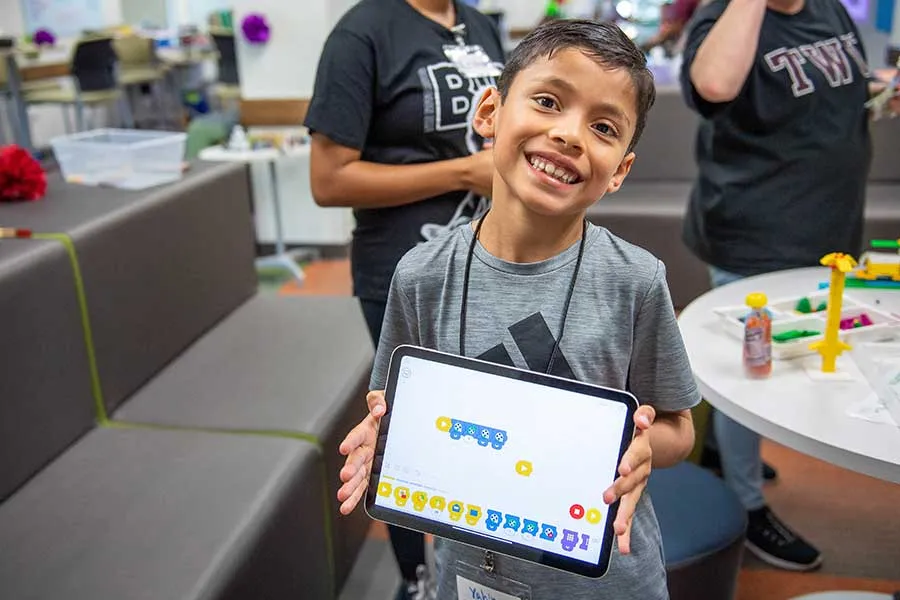 young boy holds up an Ipad showing an illustration he made