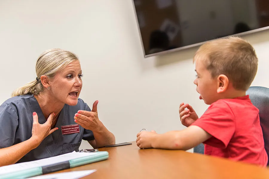 A speech-language pathology supervisor works with a young child at a table