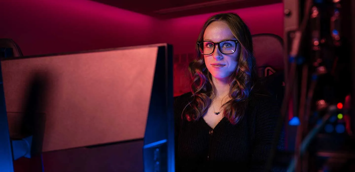 A TWU student sits at a computer with dramatic maroon and blue light on her.