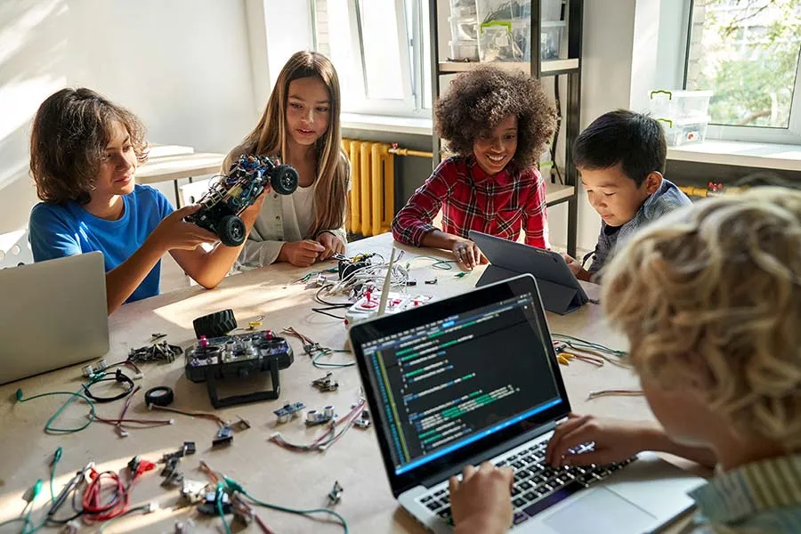 A group of kids work together building small remote-controlled robots and writing code to run them.