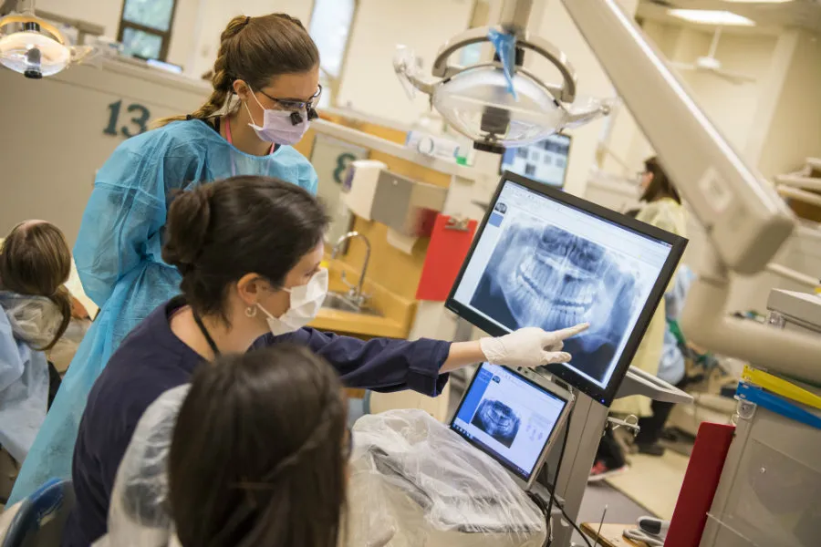 A TWU professor assists a student with reading teeth X-rays with a patient in a dentists office setting.