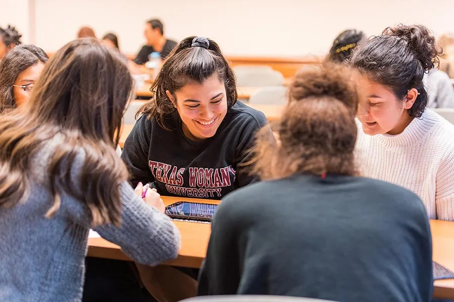A group of students chatting together in a classroom at a communal table