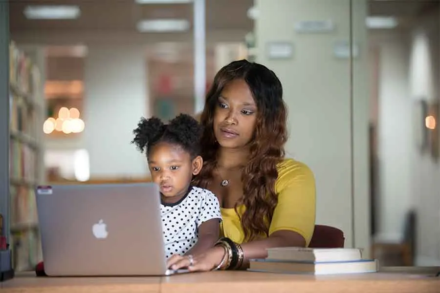 A woman works on a computer with her child in her lap.