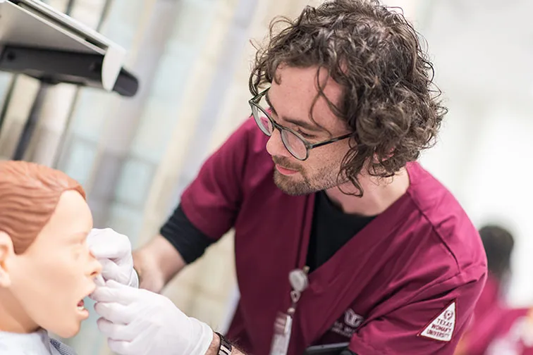 A TWU nursing student practices taking vitals on a training manikin