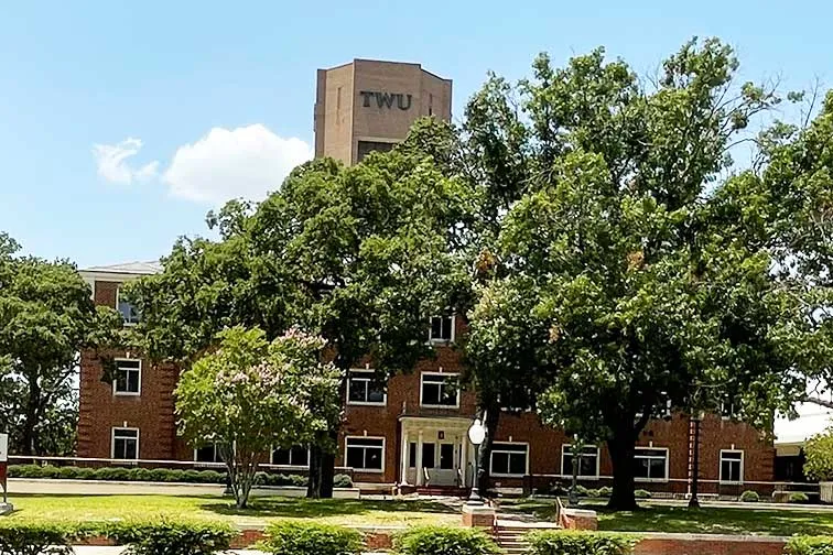 photo of Stoddard Hall building with green trees and ACT Tower with TWU