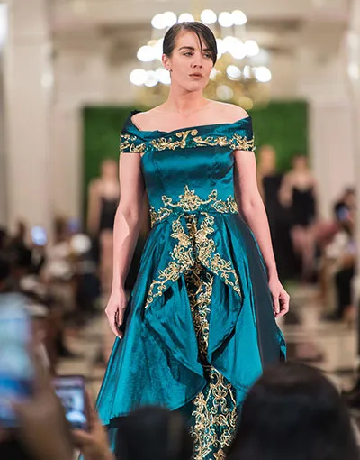 A model in a blue and gold gown walks down a fashion runway