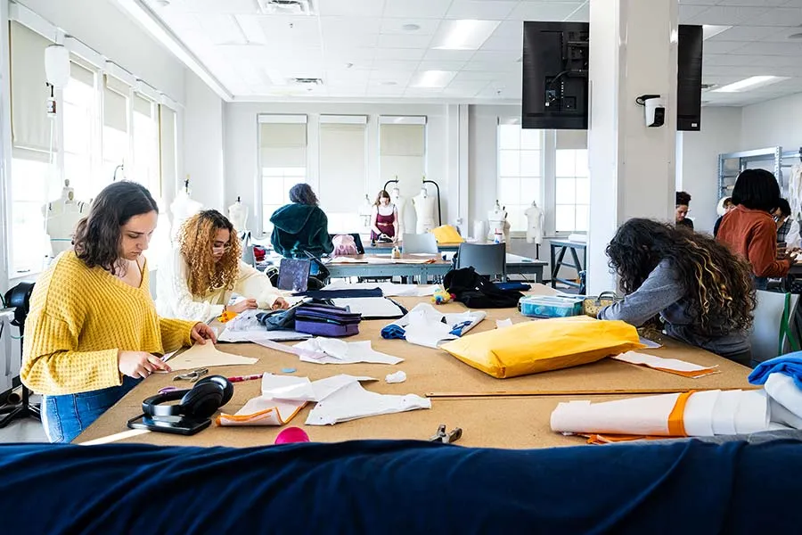 A group of people gathered around a large community worktable making and altering patterns