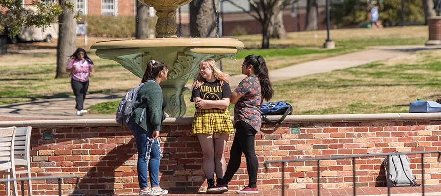Students lounge outdoors around the fountain on the TWU Denton campus.
