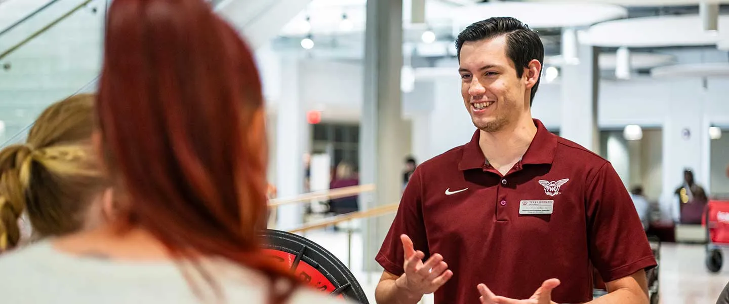 A TWU admissions counselor speaks to two prospective students at an event.