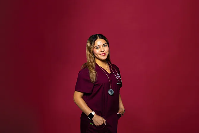 A determined looking TWU student portrait on a maroon background and dressed in nursing scrubs.