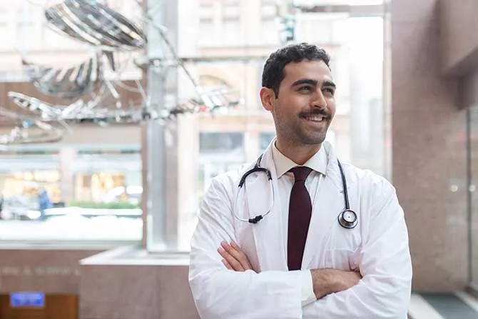 A man in a hospital setting wearing a labcoat and stethescope.