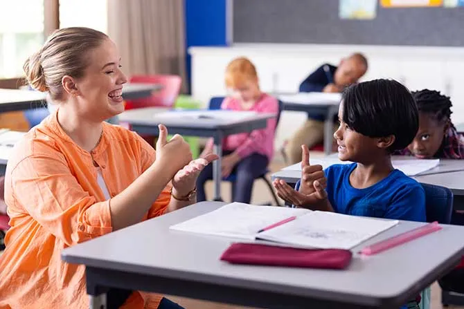 A teacher works in a classroom with a child and the are speaking sign language to each other.