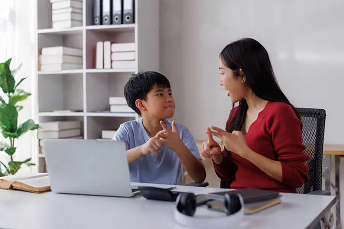 A child works with a tutor in a one-on-one session and speak sign language to each other.