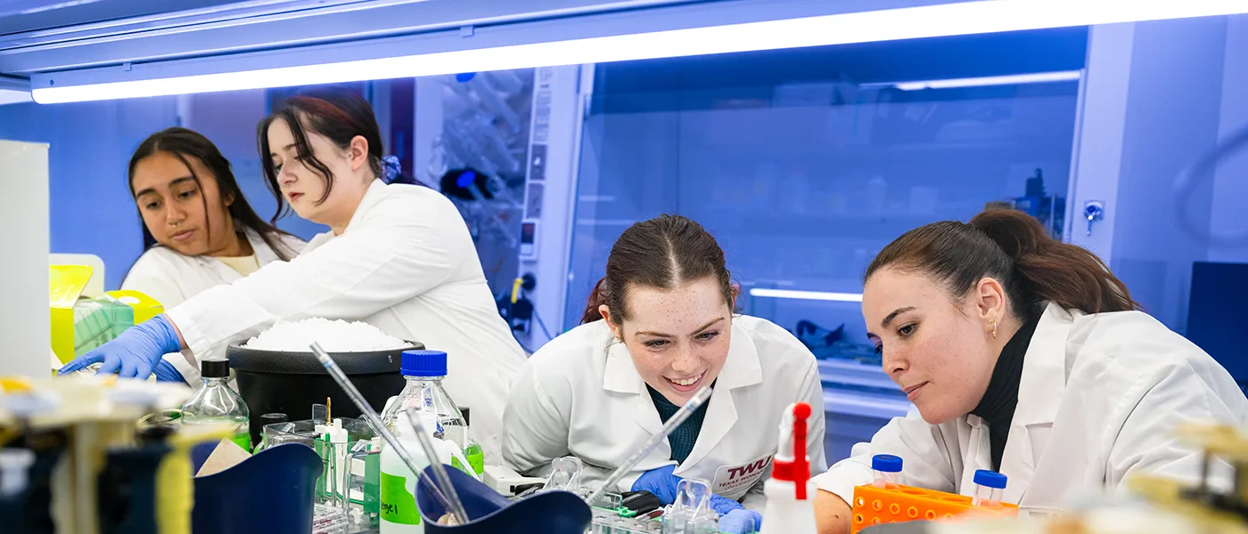 Four TWU students in a science lab and wearing labocats.