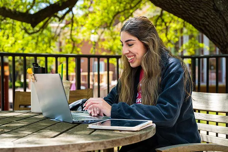 A TWU student on a laptop working outside.
