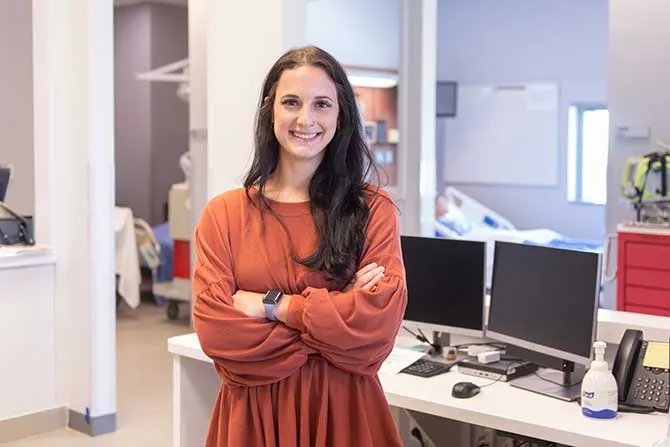 A woman stands in a hospital setting dressed in professional attire.