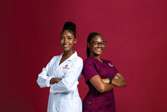 Two TWU students, one dressed in scrubs and one in a healthcare labcoat, smile for a portrait on a maroon background.